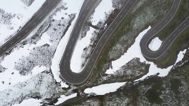Top down Aerial drone footage of the Nufenen pass in late spring during a light snowfall between the Canton Wallis and Ticino in the alps in Switzerland. 