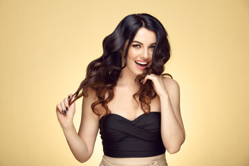 Fototapeta premium Cheerful woman with a luxurious brunette holds her hair on a yellow isolated background. Happy female portrait.