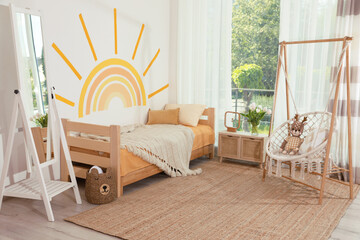 Cute child's room interior with bed, swing chair and sun art on wall