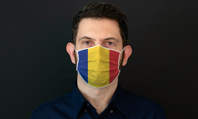 Man wearing Romanian flag protective medical face mask. He looks worried and concerned. Coronavirus concept in Romania with black background.