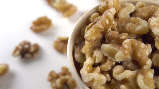 A full paper cup with peeled fresh walnut kernels on a white surface with scattered nuts. Rotation. Healthy natural snack