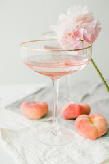 Beautiful glass with pink champagne, peaches on the background. Peonies. Aesthetic.