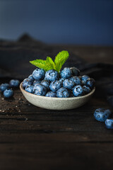 Ripe juicy blueberries with mint leaves and drops of water in a ceramic bowl on an old wooden table. Healthy food, vegetarian concept, rustic style, top view. Freshly picked blueberries.