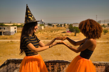 Young Hispanic and Latina women doing hand clapping games and dressed up for Halloween outdoors.