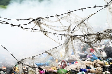 Barbed wire fence around open landfill site with burning waste. Burning pile of illegal garbage...