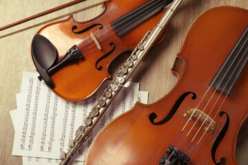 Violin, violoncello, flute and note sheets on wooden background, flat lay. Musical instruments