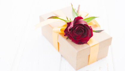 Dark red rose and gift box on white wooden background