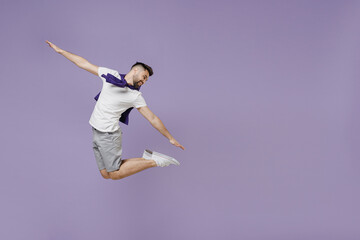 Full size body length happy fun young brunet man 20s wear white t-shirt purple shirt jump like flying look back isolated on pastel violet background studio portrait. People emotions lifestyle concept.