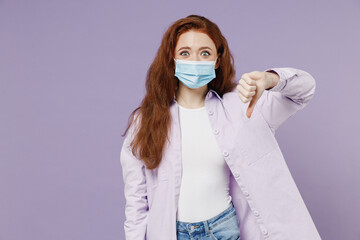 Young redhead woman 20 wear white T-shirt violet jacket sterile face mask ppe to safe from covid-19 flu show thumb down dislike gesture isolated on pastel purple color wall background studio portrait