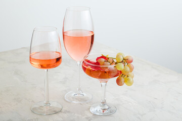 Rose wine and summer drinks champagne cocktail with grapes at wine tasting. Group glasses of pink wine on gray background. Rose wine variety minimal layout with copy space.