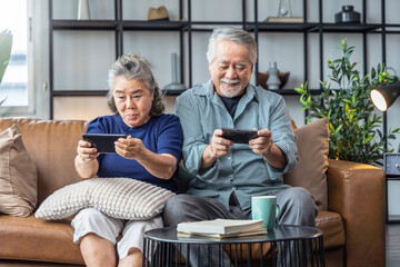 happiness asian retired couple enjoy playing and competition game smartphone mobile online together on sofa in living room home interior background,asian couple playing game together home isolate idea