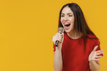 Side view profile excited magnificent beautiful overjoyed young brunette woman 20s wears basic red t-shirt sing song in microphone keep mouth wide open isolated on yellow background studio portrait.
