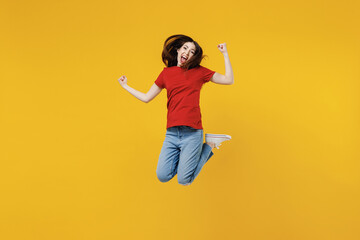 Obraz premium Full size body length excited young brunette woman 20s wears basic red t-shirt jump doing winner gesture celebrating isolated on yellow background studio portrait. People emotions lifestyle concept