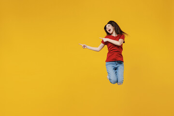 Fototapeta na wymiar Full size body length young brunette woman 20s wear basic red t-shirt jump point aside away on workspace area copy space mock up isolated on yellow background studio portrait. People emotions concept