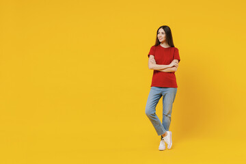 Fototapeta na wymiar Full size body length excited young brunette woman 20s wear basic red t-shirt stand hold hands crossed look aside away isolated on yellow background studio portrait. People emotions lifestyle concept