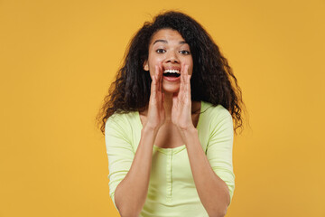 Promoter african american young woman 20s wears green shirt scream hot news about sales discount with hands near mouth isolated on yellow background studio portrait. People emotions lifestyle concept