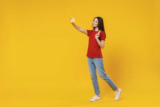 Full size body length young brunette woman 20s wears basic red t-shirt do selfie shot on mobile cell phone post photo on social network show victory sign isolated on yellow background studio portrait