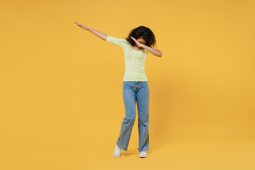 Full size body length slim sporty african american young woman 20s wears green shirt doing dab hip hop dance hands move gesture youth sign hide cover faceisolated on yellow background studio portrait