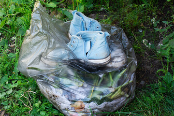 Pair old dirty blue sneakers in black garbage bag on green grass background.
