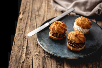 chocolate and cream profiteroles on rustic wooden table. Copy space