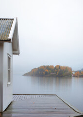 White vintage cabin  by the sea coast with wet pier . Foliage gold colors. Rainy , foggy day. Blurred background. Southern Norway