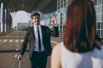 Young happy traveler businessman man 20s wearing black dinner suit walk go outside at international...