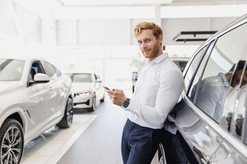 Man happy customer male buyer client wear white shirt talk by mobile cell phone leaning on car choose auto want buy new automobile in showroom vehicle dealership store motor show indoor Sales concept