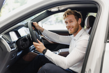 Smiling happy man customer buyer businessman client wear classic suit sit in car salon chooses auto...