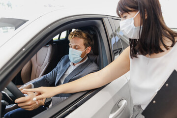 Man customer buyer client wear grey suit pandemic masks drive car choose auto want buy new automobile in showroom consult with salesman vehicle salon dealership store motor show indoor Sale concept.