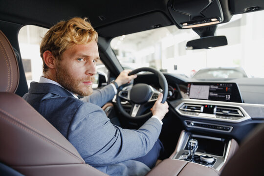 Side view serious businessman blond man driver male cabdriver in classic grey suit driving car hold wheel in traffic jam look camera test auto want buy new automobile vehicle Sale transport concept