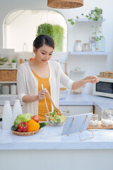 Beautiful young woman with tablet computer cooking in kitchen