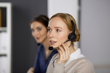 Friendly businesswoman talking by headset while sitting in office. Call center and diverse people...