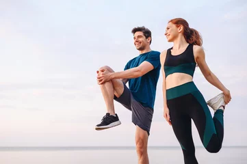  Lower couple young two friend strong sporty sportswoman sportsman woman man in sport clothes warm up training do stretch exercise on sand sea ocean beach outdoor jog on seaside in summer day morning. © ViDi Studio