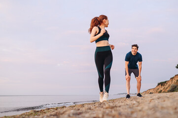 Full size lower couple young two friends strong sporty sportswoman sportsman woman man wear sport clothes warm up training running on sand sea ocean beach outdoor jog on seaside in summer day morning.
