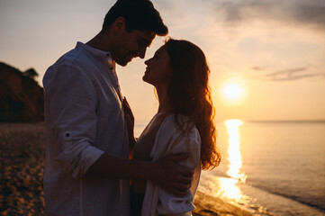 Fototapeta premium Side view silhouette happy young couple two friends family man woman 20s in white clothes hug going to kiss other together at sunrise over sea beach ocean outdoor seaside in summer day sunset evening