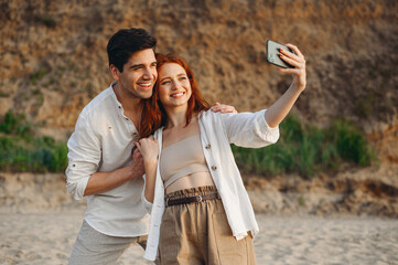 Young couple two friends family man woman in white clothes hug rest together do selfie shot mobile cell phone post photo social network at sunrise over sea sand beach outdoor seaside in summer day