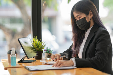 Businesswoman with face mask surfing the net on a tablet in a cafe.