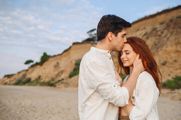 Side view close up smiling happy young tender couple two friends family man woman in casual clothes hug each other kiss forehead at sunrise over sea beach outdoor seaside in summer day sunset evening