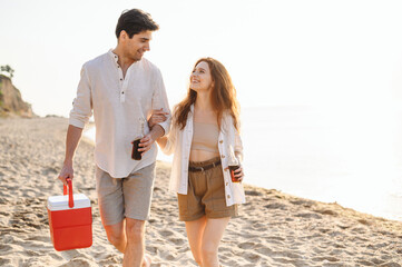 Happy young couple two friend family man woman in white clothes drink beer hold bag refrigerator have picnic rest together at sunrise over sea beach ocean outdoor seaside in summer day sunset evening. - Powered by Adobe