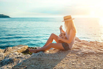 Summer Vacation. Smellingcaucasian women relaxing and playing on ukulele on beach, so happy and luxury in holiday summer, outdoors sunset sky background. Travel and lifestyle Concept.