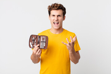 young handsome man looking angry, annoyed and frustrated and holding a nails tools case
