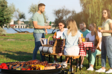 Group of friends having party outdoors, focus on barbecue grill with food