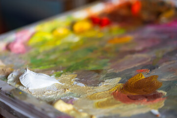 Artist's palette with white oil paint close-up. Blurry multicolored background. Professional paints of the artist in a selective focus. The concept of creativity, creative ideas, a favorite hobby.