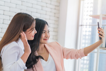 Beautiful young business women are selfie with her friend by cellphone or smartphone at living room. Happy friendship relationship concept