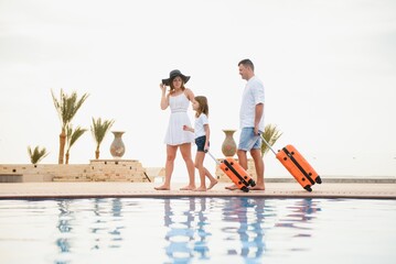 young family with suitcases walking to hotel building with beautiful swimming pool. traveling and...