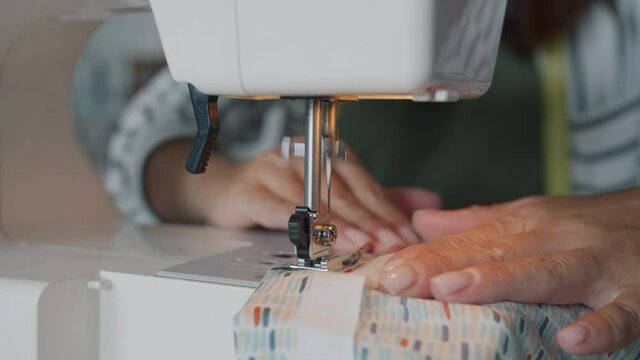 Close-up footage of female hand working with modern electric sewing machine stitching piece of textile making garment. People and profession concept.