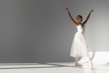Fototapeta na wymiar Young ballerina in white dress dancing on grey background