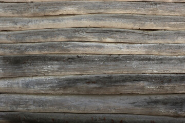 The wall of an old wooden house made of darkened weathered logs. Texture of old vintage wooden planks background natural.