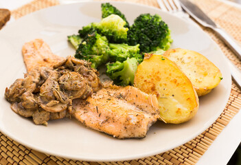 fried river trout fillet with a complex side dish of broccoli, baked potatoes and mushroom sauce