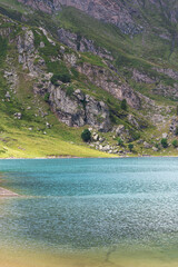Mountain lake in the middle of the alps. Summer in the green mountain with a blue lake. Alpine mountains with a play of light and shadow of the clouds.